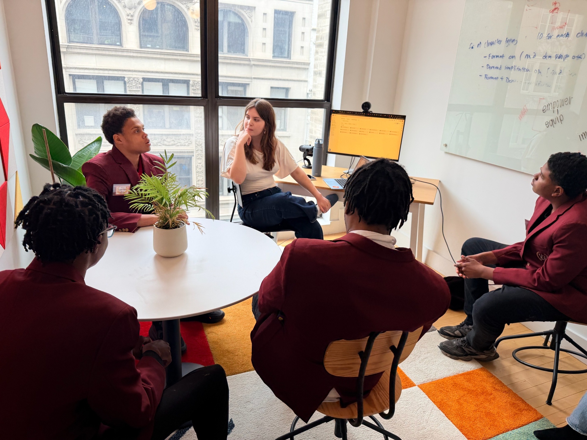 Small roundtable discussion in a NYC office, with Dixie leading conversation with a group seated around a white table