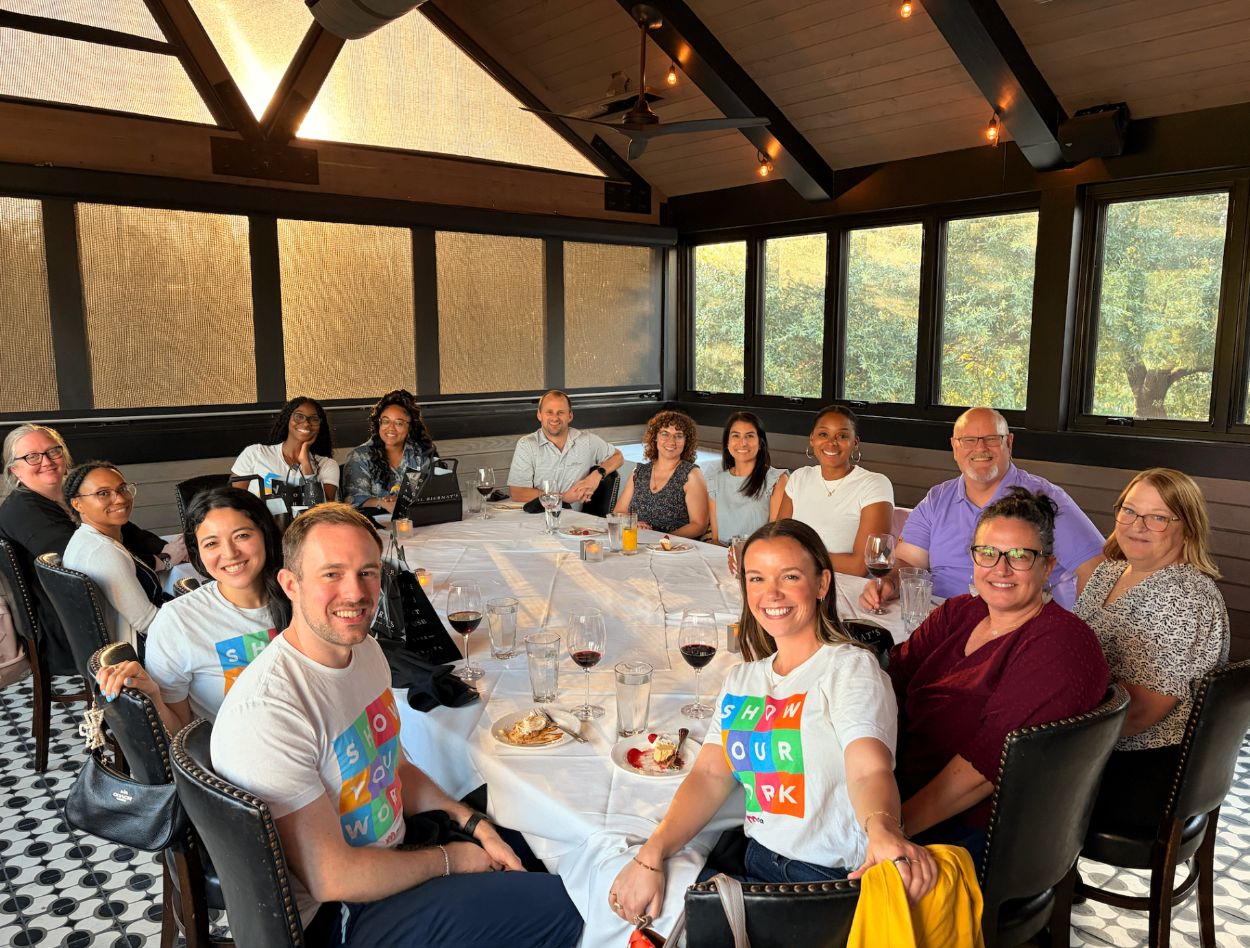 Team celebratory dinner around a large round table, with guests wearing matching colorful event t-shirts