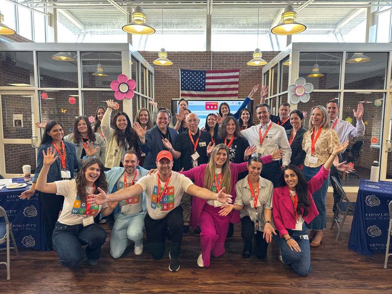 Large group of event attendees waving and cheering together in a bright conference space with an American flag behind them